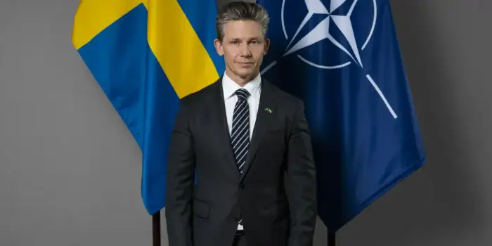 Porträtt på Pål Jonson med svenska flaggan och Natos flagga i bakgrunden