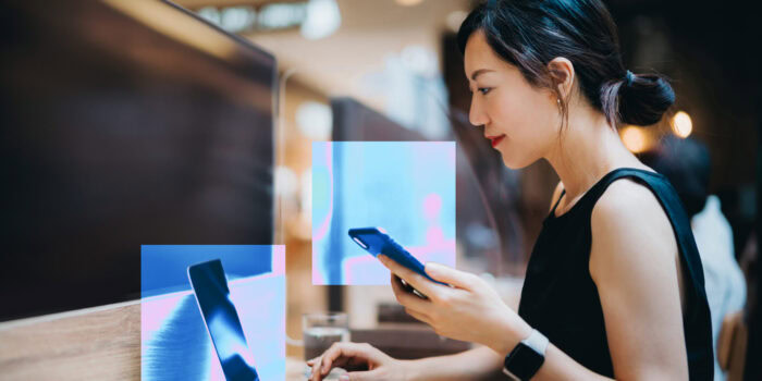 A woman looks at her computer screen and holds a phone in her left hand