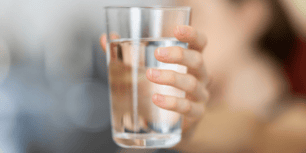 Närbild på en hand som håller ett glas med klart dricksvatten.