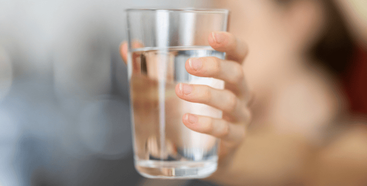 Närbild på en hand som håller ett glas med klart dricksvatten.