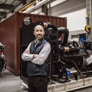 Kim Nilsson framför ett reservkraftaggregat inne i nya produktionsanläggningen. Foto från Coromatic.
